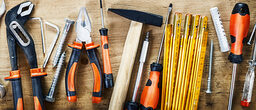Auf einer Holzplatte liegen verschiedene Werkzeuge wie Hammer, Zange, Schraubendreher etc.