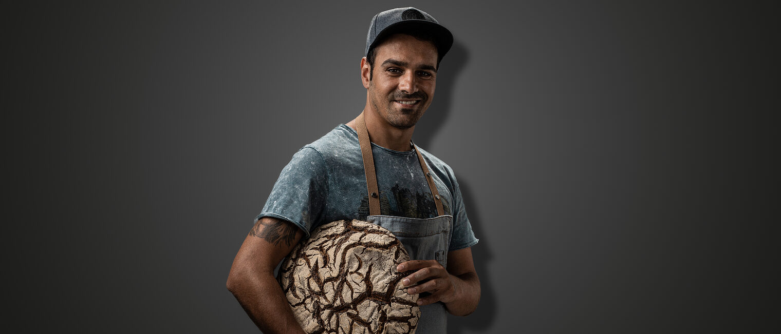 Bäckermeister Taner Karadagli posiert mit einem rundem Brot in die Kamera 