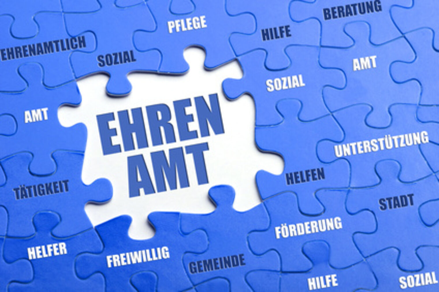 Puzzelteile in blau gehalten mit verschiedenen Wörtern wie Amt, Helfer, Hilfe. Ein Weißes Puzzelteil mit dem Wort Ehrenamt