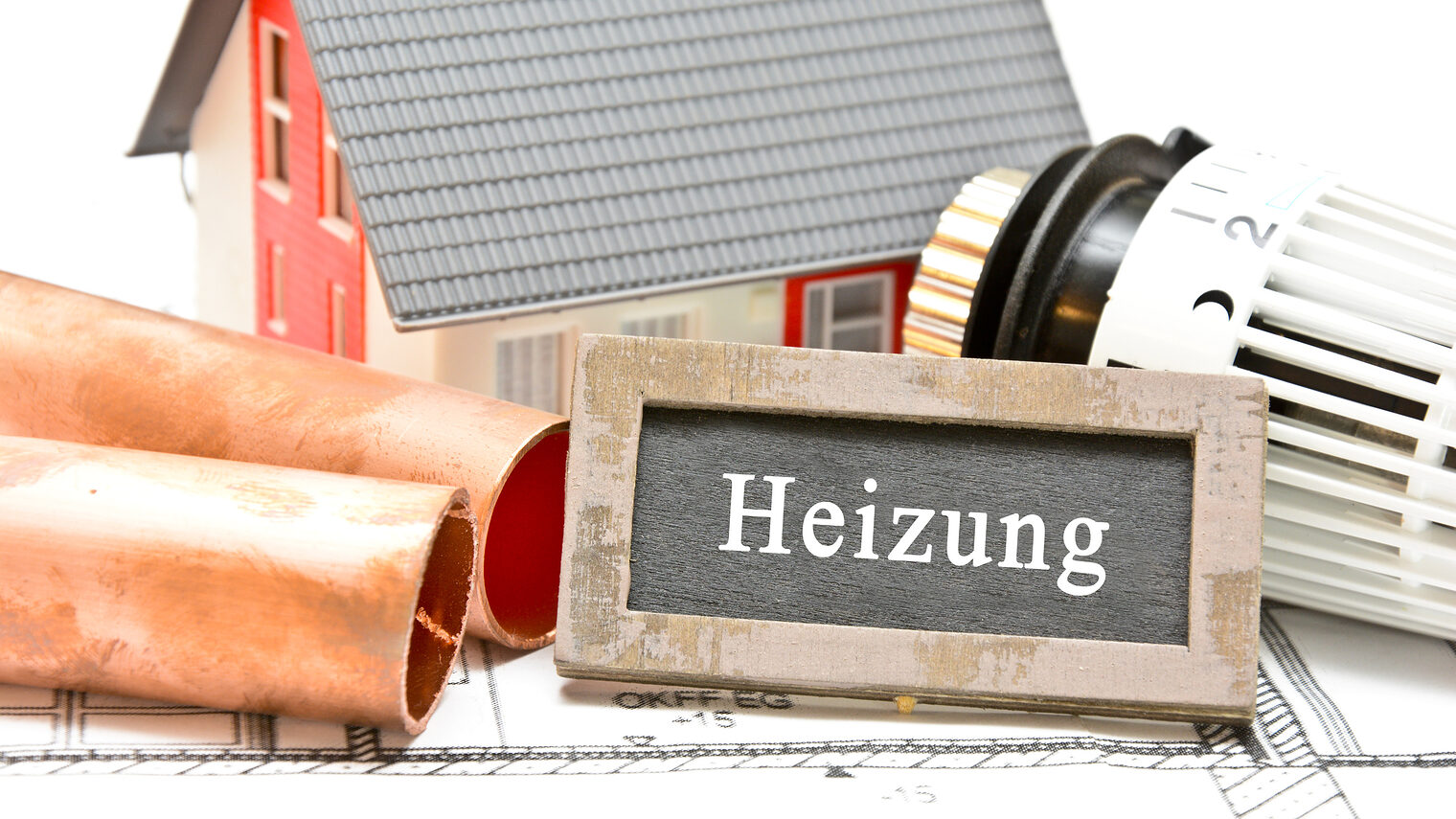 Schriftzug "Heizung" im Hintergrund ist ein kleines Haus, ein durchgeschnittetens Rohr und ein Thermostat-Kopf