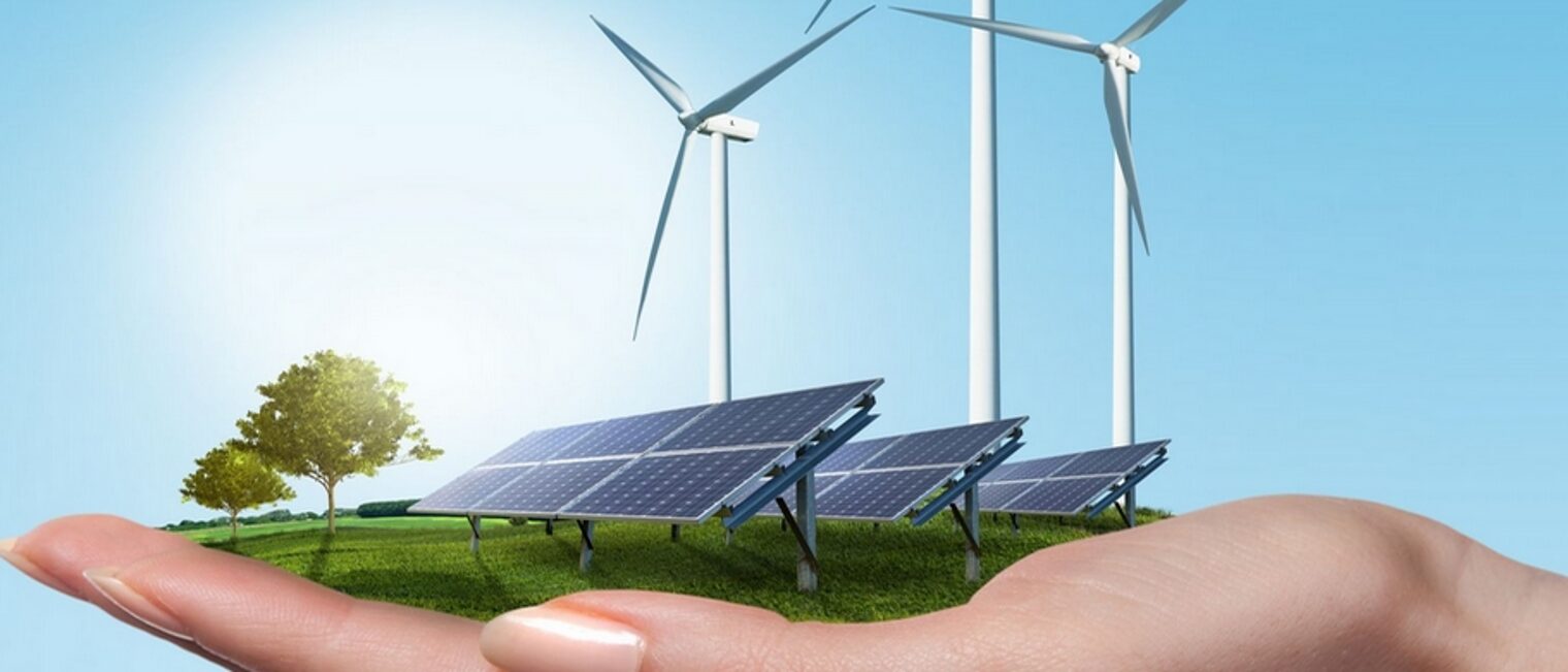 Auf einer Handfläche in Miniatur eine Landschaft mit Solarpanelen und Windkrafträdern vor einem hellblauen Hintergrund.