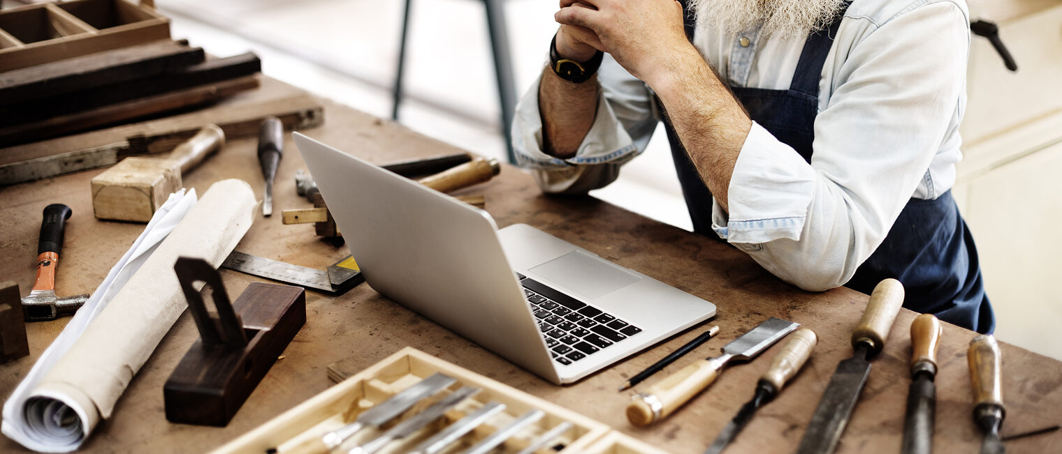 Handwerk 2025 Schreiner Ein Mann sitzt an einem Arbeitstisch. Auf dem Tisch befindet sich sehr viel Werkzeug und ein Laptop