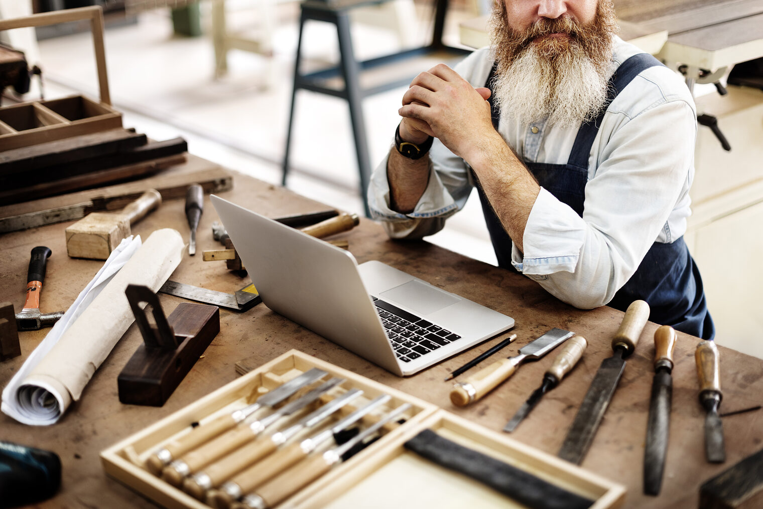 Ein Mann sitzt an einem Arbeitstisch. Auf dem Tisch befindet sich sehr viel Werkzeug und ein Laptop 