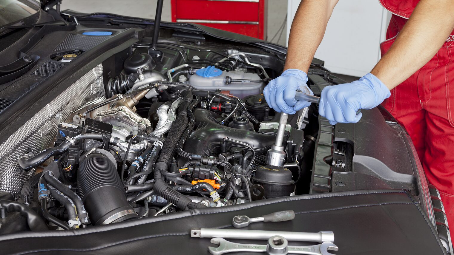 Ein Mann mit blauen Handschuhen schraubt an einem Motor