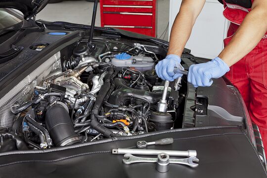 Ein Mann mit blauen Handschuhen schraubt an einem Motor