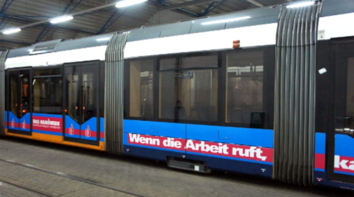 Straßenbahn, die mit Werbung aus der Imagekampagne versehen ist. Text der Werbung: Wenn die Arbeit ruft, kaum zu bremsen.
