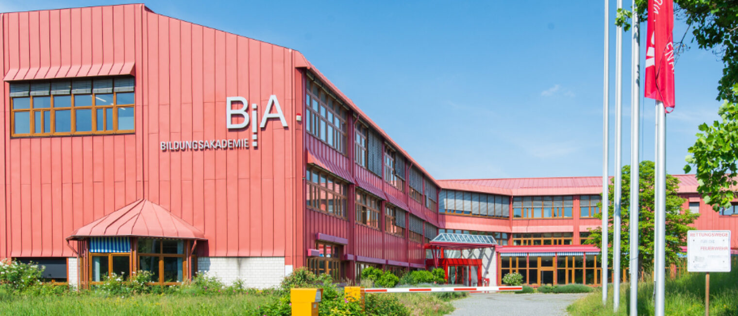 BiA - Bildungsakademie. Haus in rot gehalten und mit Fahnenstangen im Eingangsbereich