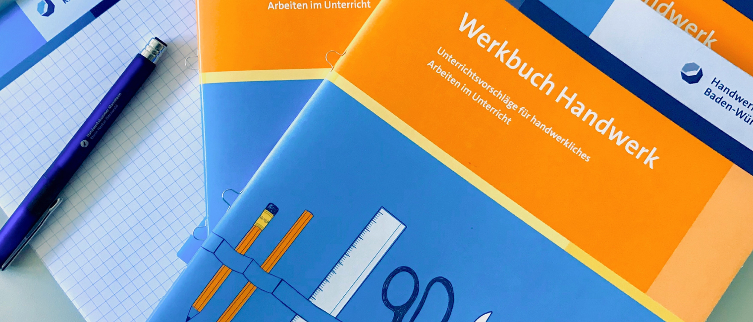 Werkbuch Handwerk Auf einem karierten Handwerkskammerblock liegen ein Stift und zwei Ausgaben der Unterrichtsbroschüre Werkbuch Handwerk