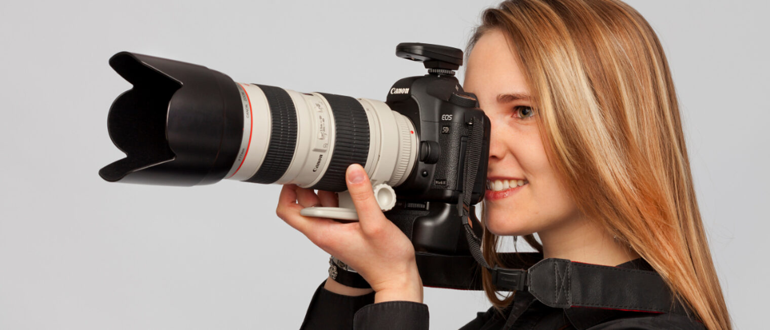 Fotografin hält eine Kamera mit großem Objektiv in der Hand.
