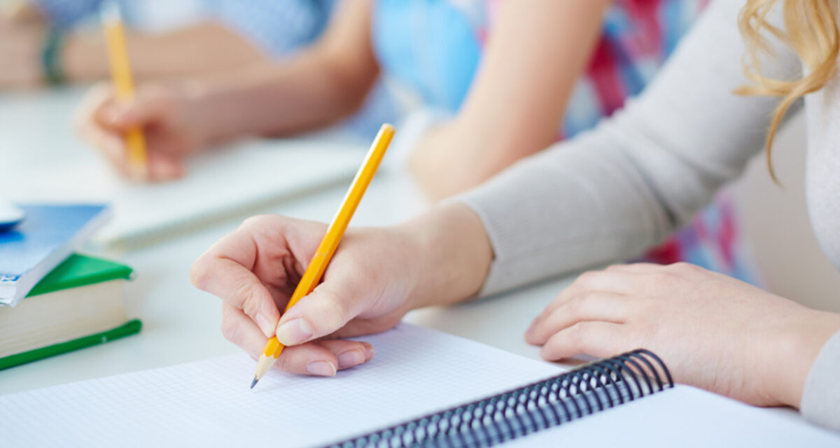 Personen schreiben im Unterricht Notizen in ihr Ringbuch. Zu sehen sind nur die schreibende Hand, Arm und Block.