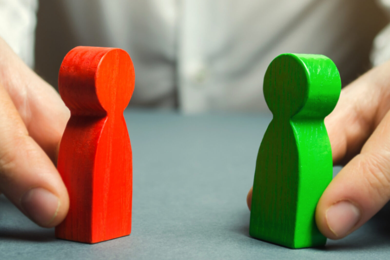 Eine rote und eine grüne Spielfigur werden von einer Person mit den Händen so festgehalten, dass nur die Hände und die Spielfiguren deutlich zu sehen sind.