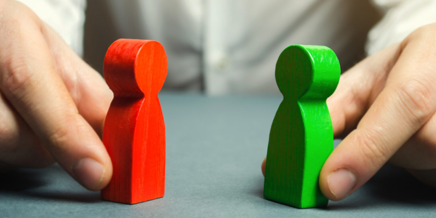 Eine rote und eine grüne Spielfigur werden von einer Person mit den Händen so festgehalten, dass nur die Hände und die Spielfiguren deutlich zu sehen sind.