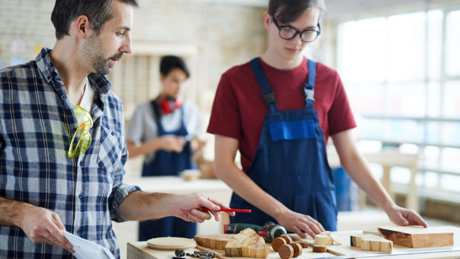 Prüfer begutachtet das Werkstück eines Auszubildenden im Tischlerhandwerk 