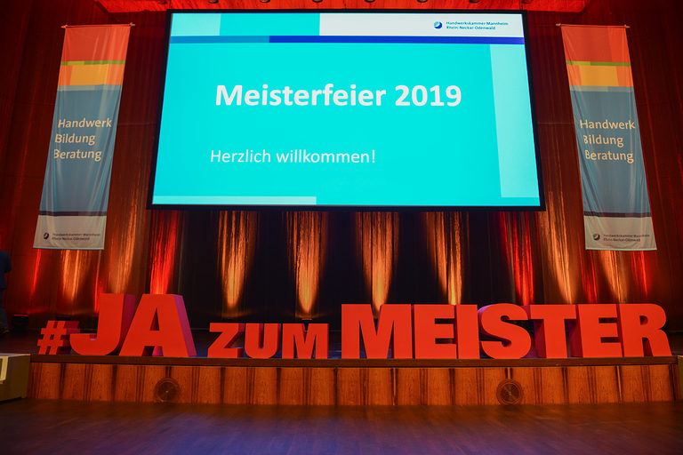 Foto der Bühne der Meisterfeier 2019 im Congresscenter Rosengarten in Mannheim 2019. Zu sehen ist ein großes Schriftzu "#JAzumMEISTER" und die Bühnenleinwand. 