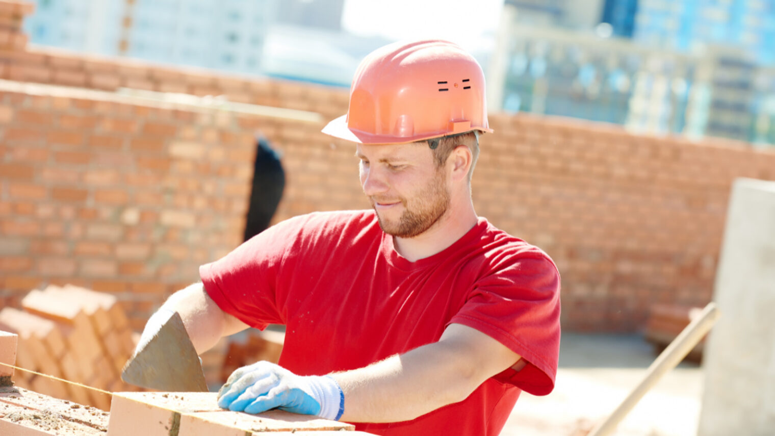 Bauarbeiter mit rotem T-Shirt und Helm in der Farbe orange zieht eine Mauer hoch