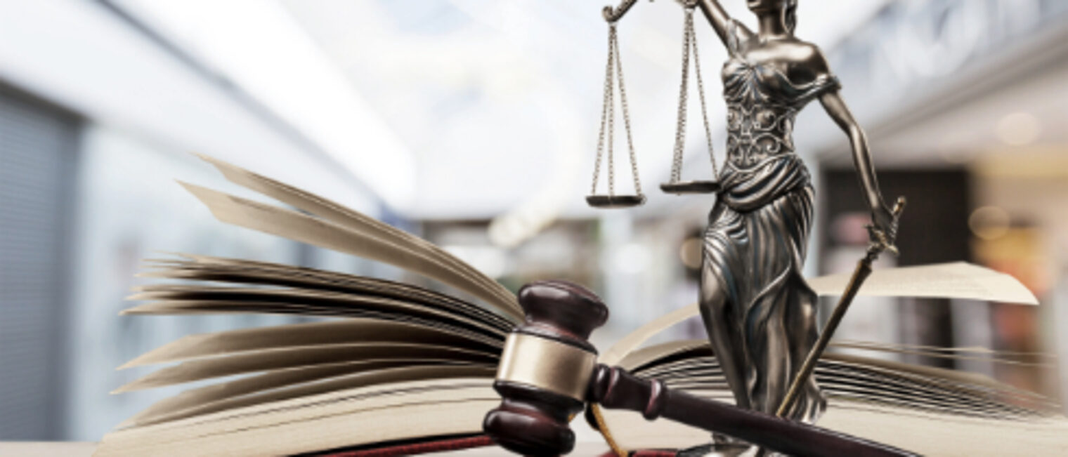 Rechtliche Infos für Betriebe Ein offenes Buch, ein Hammer und eine Justitia Figur mit Waage auf einem Tisch