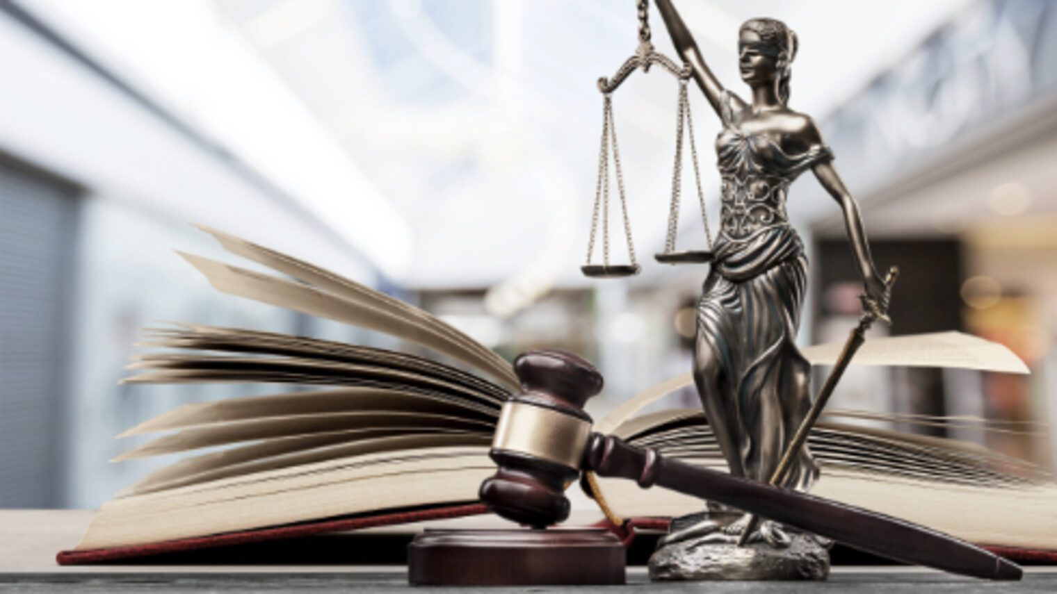 Ein offenes Buch, ein Hammer und eine Justitia Figur mit Waage auf einem Tisch
