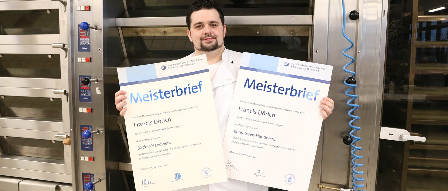 Bäcker- und Konditormeister zeigt seine Meisterbriefe vor seinem Backofen.