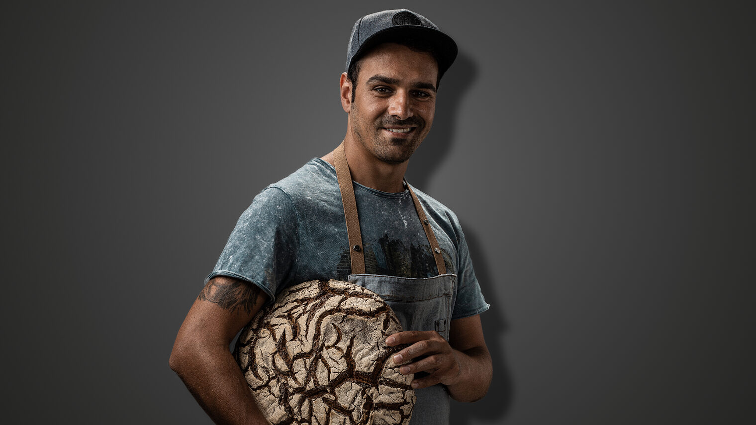Bäckermeister Taner Karadagli posiert mit einem rundem Brot in die Kamera 