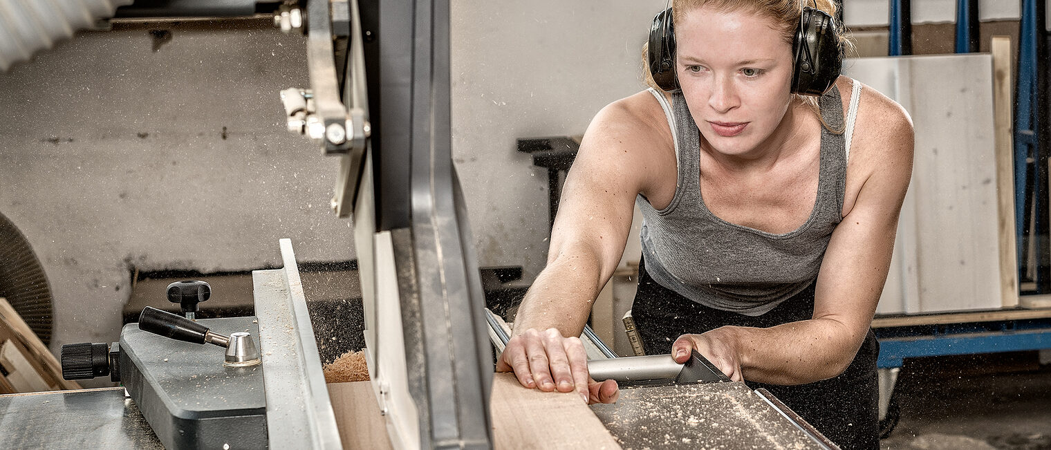 Eine Frau schneidet an einer Maschine ein stück Holz 