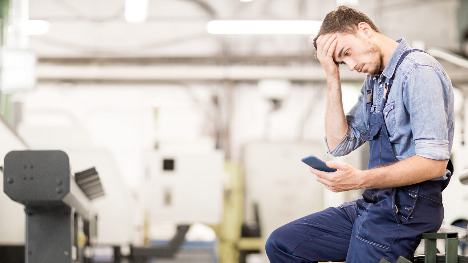 Mann sitz in der Werkstatt und schaut auf sein Handy.