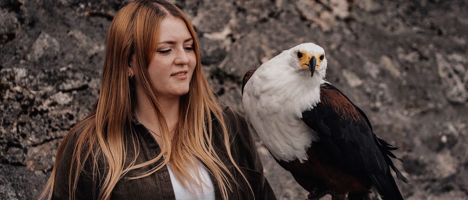 Felicitas Rieger - Falknereibedarf und Lederwerkstatt Sattlerin und Feintäschnerin Felicitas Rieger steht im freien und hat einen Adler auf dem linken Arm. (Der Umgang mit wilden Tieren ist Feli-citas Rieger aus Neidenstein nicht fremd)