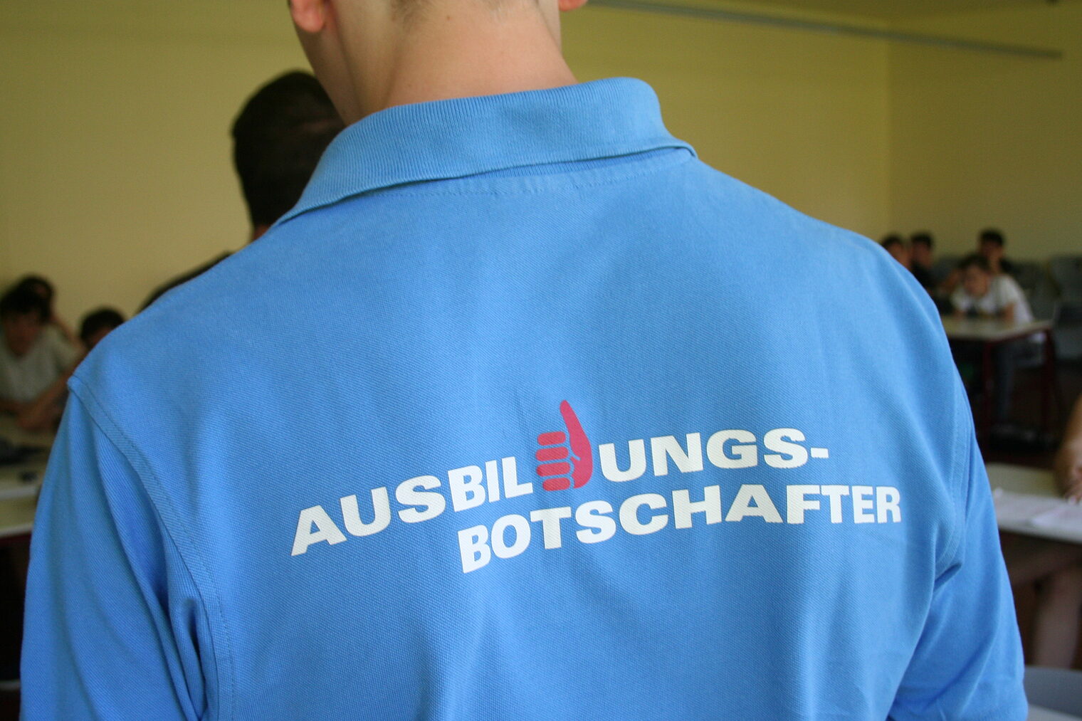 Rückenansicht eines Auszubildenden im blauen T-Schirt mit der Aufschift Ausbildungsbotschafter