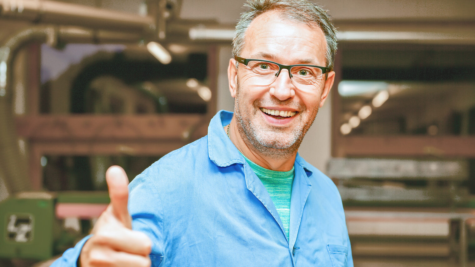 Mann mit Brille und blauem Hemd zeigt mit seiner rechten Hand den Daumen hoch.