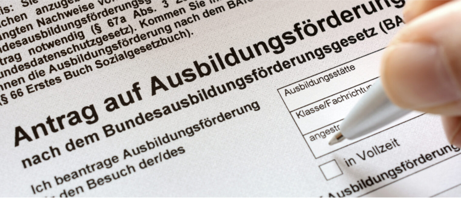 Ein Antrag auf Ausbildungsförderung mit einer Hand die diesen ausfüllt.