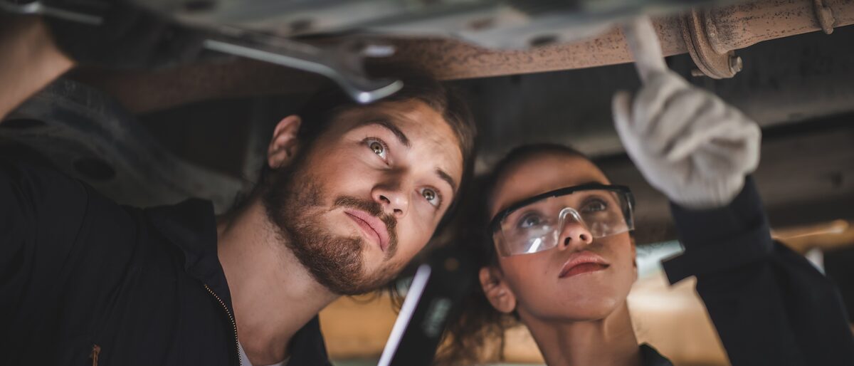 6-Tage-Crash-Kurs zur Ausbilder-Eignungsprüfung Ein Kraftfahrzeugtechniker und eine Kraftfahrzeugtechnikerin prüfen die Unterseite eines Autos.