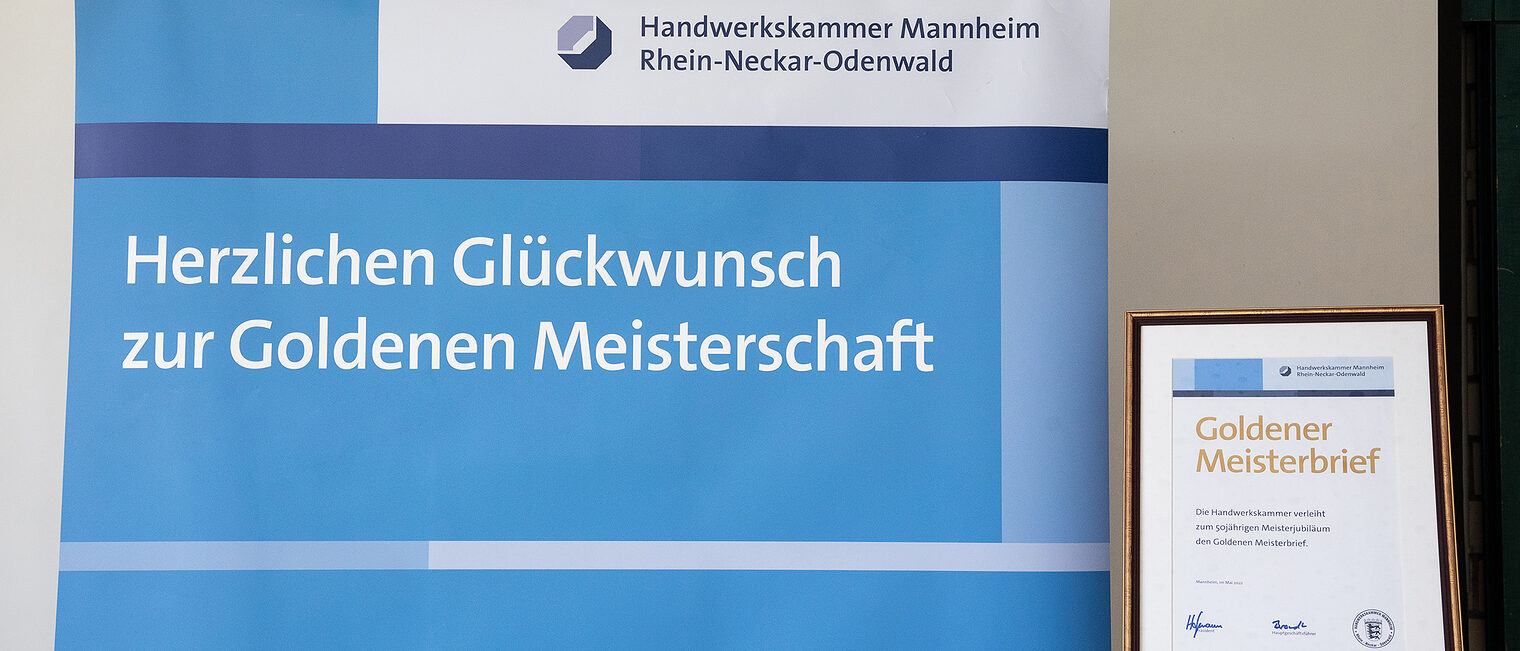 Goldene Meisterfeier 2022 - Mannheim - Roll-Up mit Schriftzug und daneben ein gerahmter goldener Meisterbrief auf einer Staffelei
