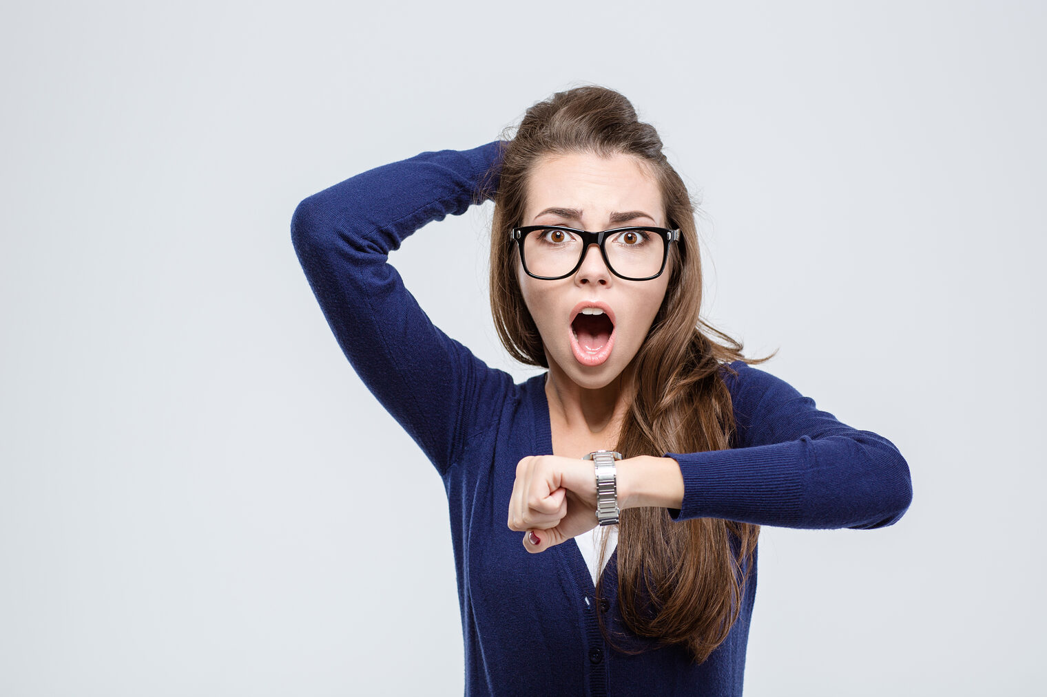 Porträt einer schockierten jungen Frau, die ihr Handgelenk mit einer Uhr hoch hält und in die Kamera blickt