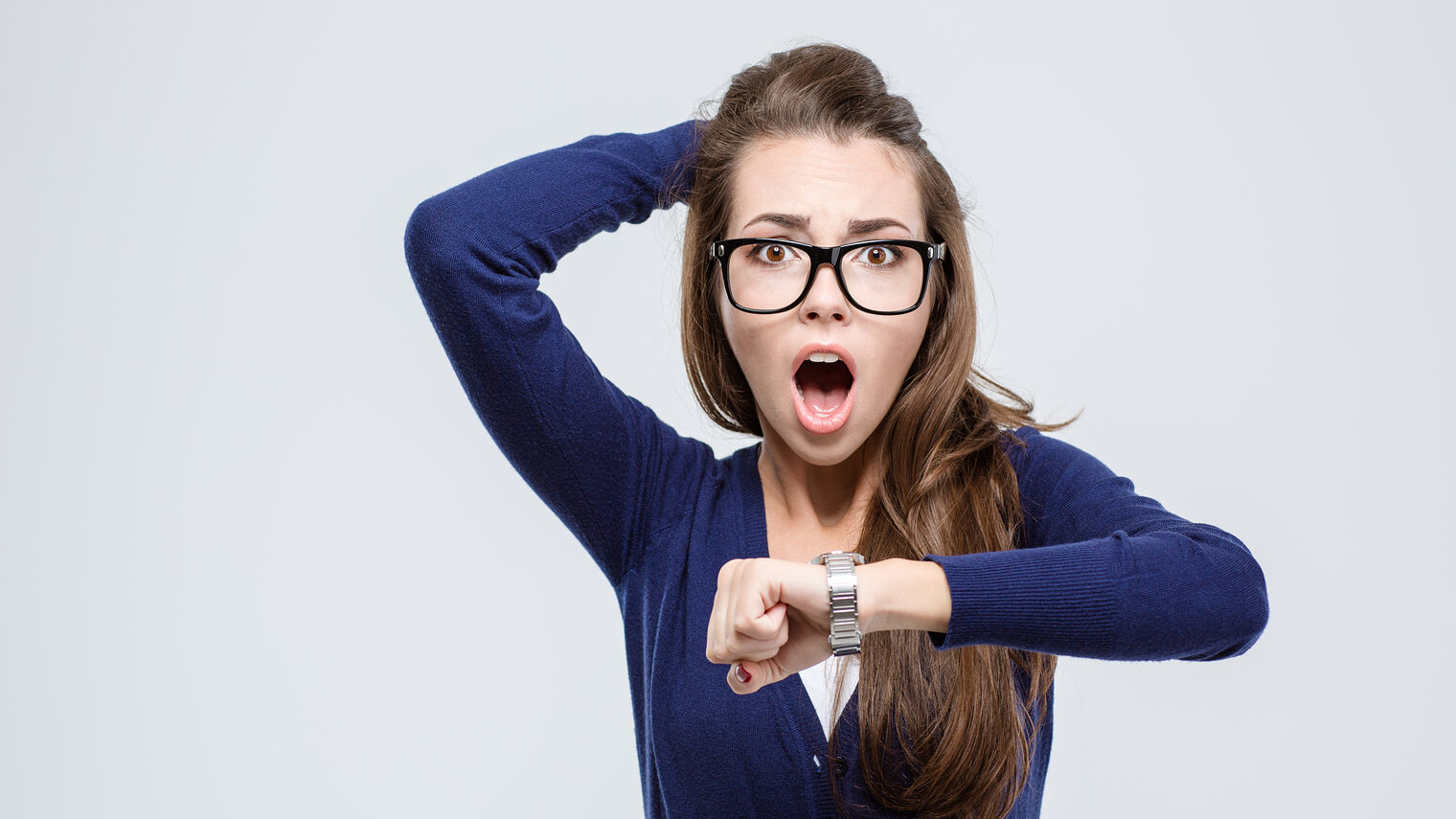 Porträt einer schockierten jungen Frau, die ihr Handgelenk mit einer Uhr hoch hält und in die Kamera blickt