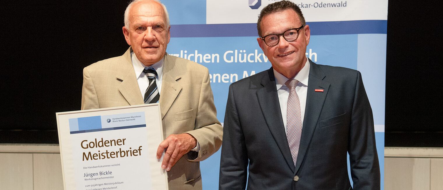 Kammerpräsident Klaus Hofmann überreicht Werkzeugmachermeister Jügren Bickle auf der Goldene Meisterfeier in Wiesloch 2022 seinen Goldenen Meisterbrief