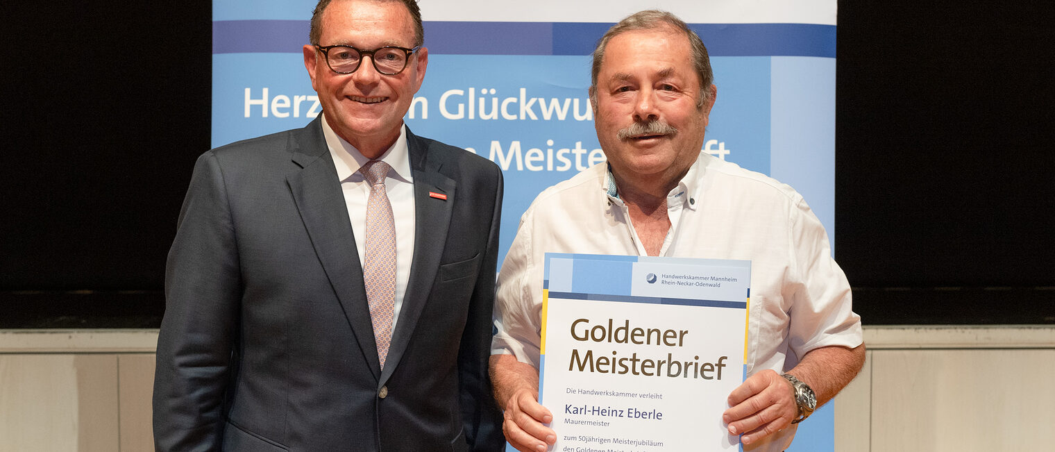 Kammerpr&auml;sident Klaus Hofmann &uuml;berreicht Maurermeister Karl-Heinz Eberle auf der Goldene Meisterfeier in Wiesloch 2022 seinen Goldenen Meisterbrief