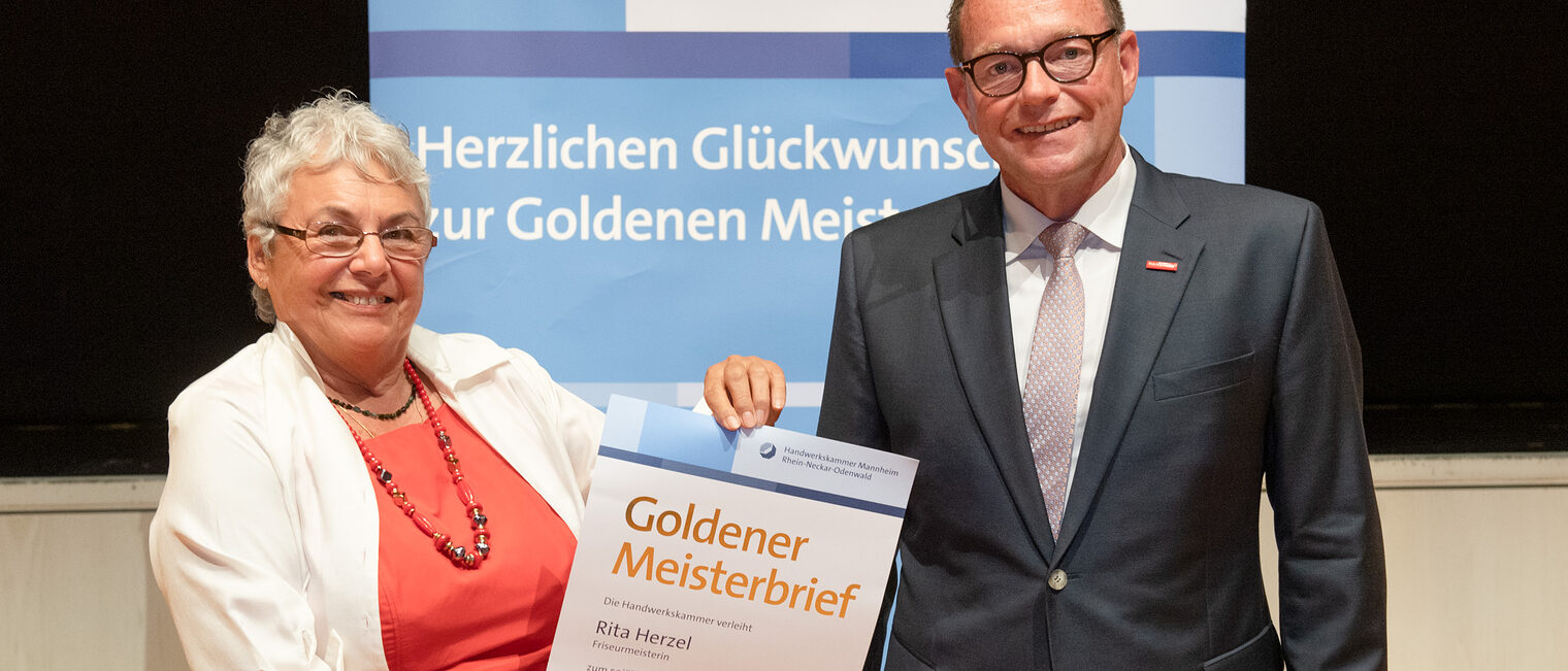 Kammerpr&auml;sident Klaus Hofmann &uuml;berreicht Friseurmeisterin Rita Herzel auf der Goldene Meisterfeier in Wiesloch 2022 ihren Goldenen Meisterbrief