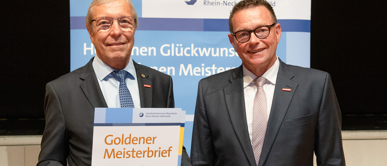 Kammerpräsident Klaus Hofmann überreicht Maler- und Lackierermeister Alois Jöst auf der Goldene Meisterfeier in Wiesloch 2022 seinen Goldenen Meisterbrief