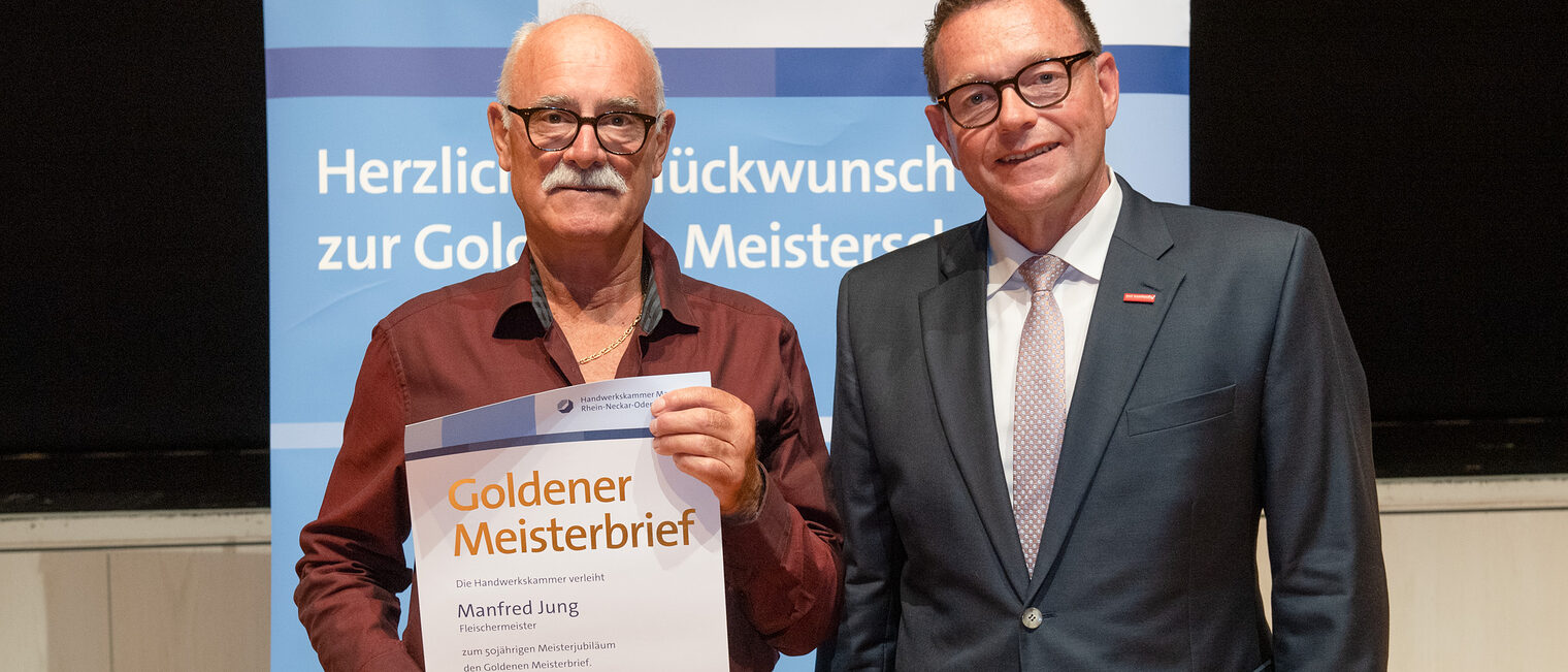 Kammerpr&auml;sident Klaus Hofmann &uuml;berreicht Fleischermeister Manfred Jung auf der Goldene Meisterfeier in Wiesloch 2022 seinen Goldenen Meisterbrief