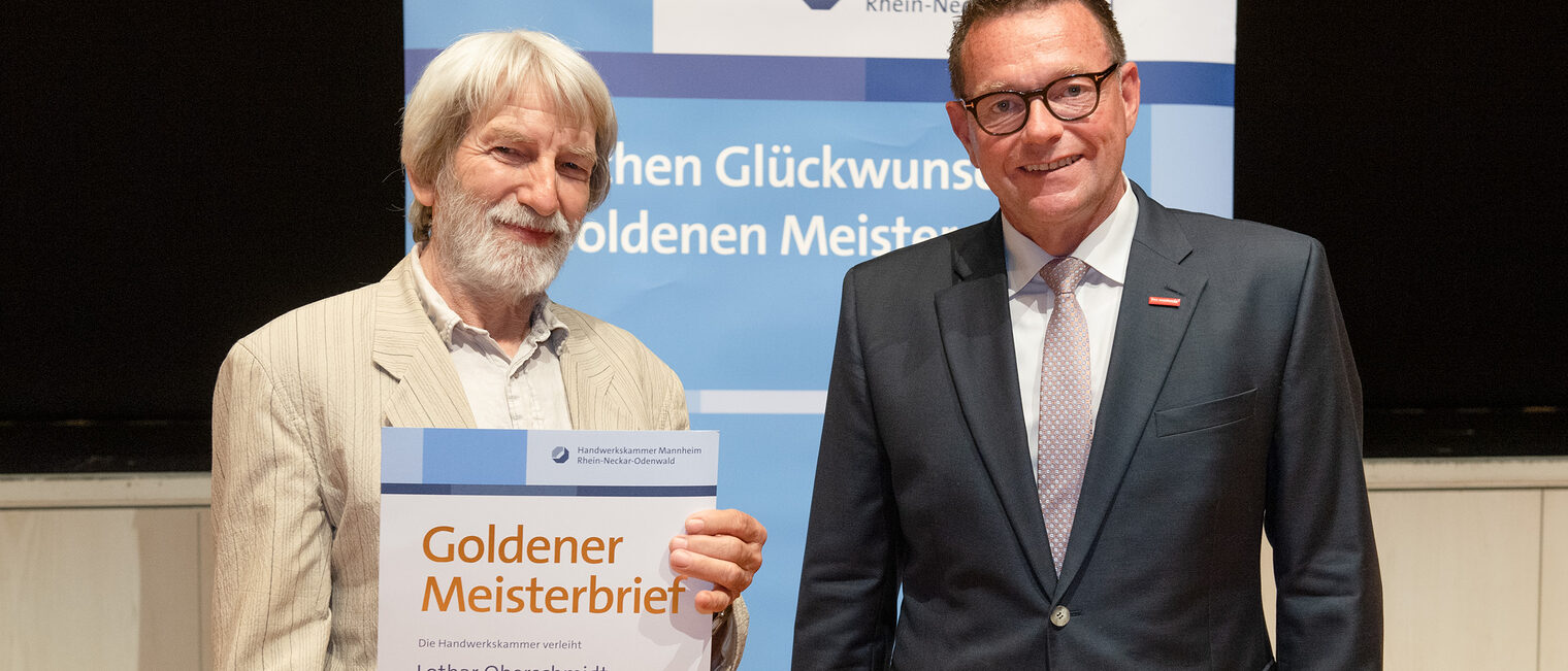 Kammerpräsident Klaus Hofmann überreicht Kraftfahrzeugmechanikermeister Lothar Oberschmidt auf der Goldene Meisterfeier in Wiesloch 2022 seinen Goldenen Meisterbrief