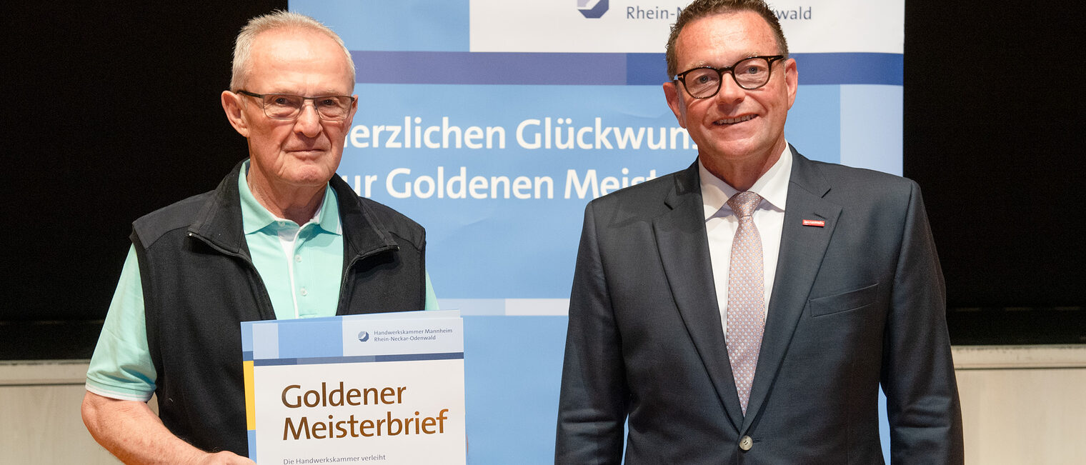 Kammerpräsident Klaus Hofmann überreicht Kraftfahrzeugmechanikermeister Rolf Petri auf der Goldene Meisterfeier in Wiesloch 2022 seinen Goldenen Meisterbrief