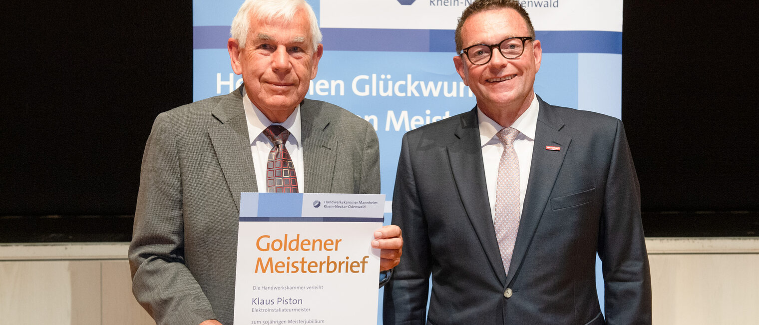 Kammerpräsident Klaus Hofmann überreicht Elektroinstallateurmeister Klaus Piston auf der Goldene Meisterfeier in Wiesloch 2022 seinen Goldenen Meisterbrief