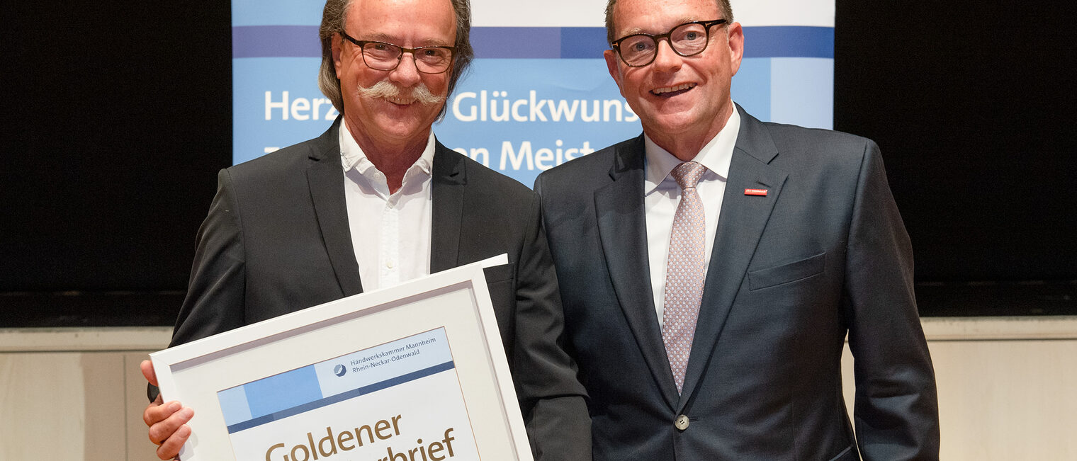 Kammerpr&auml;sident Klaus Hofmann &uuml;berreicht Friseurmeister Bernhard Schedwill auf der Goldene Meisterfeier in Wiesloch 2022 seinen Goldenen Meisterbrief