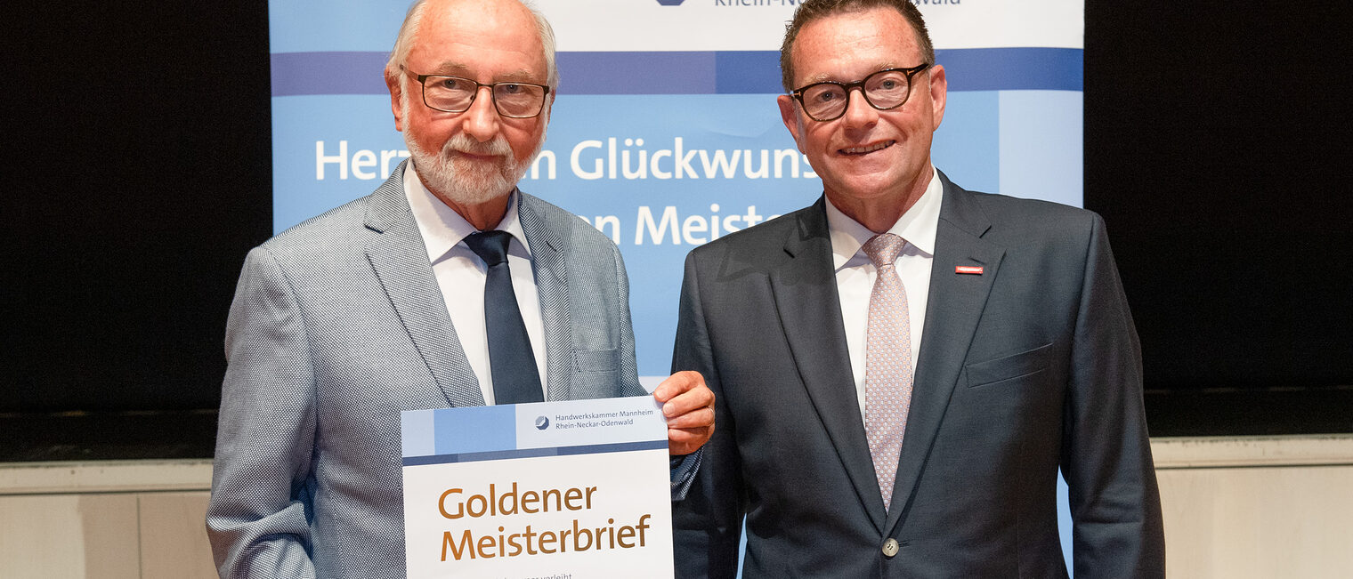 Kammerpräsident Klaus Hofmann überreicht Elektroinstallateurmeister Gerd Scherer auf der Goldene Meisterfeier in Wiesloch 2022 seinen Goldenen Meisterbrief