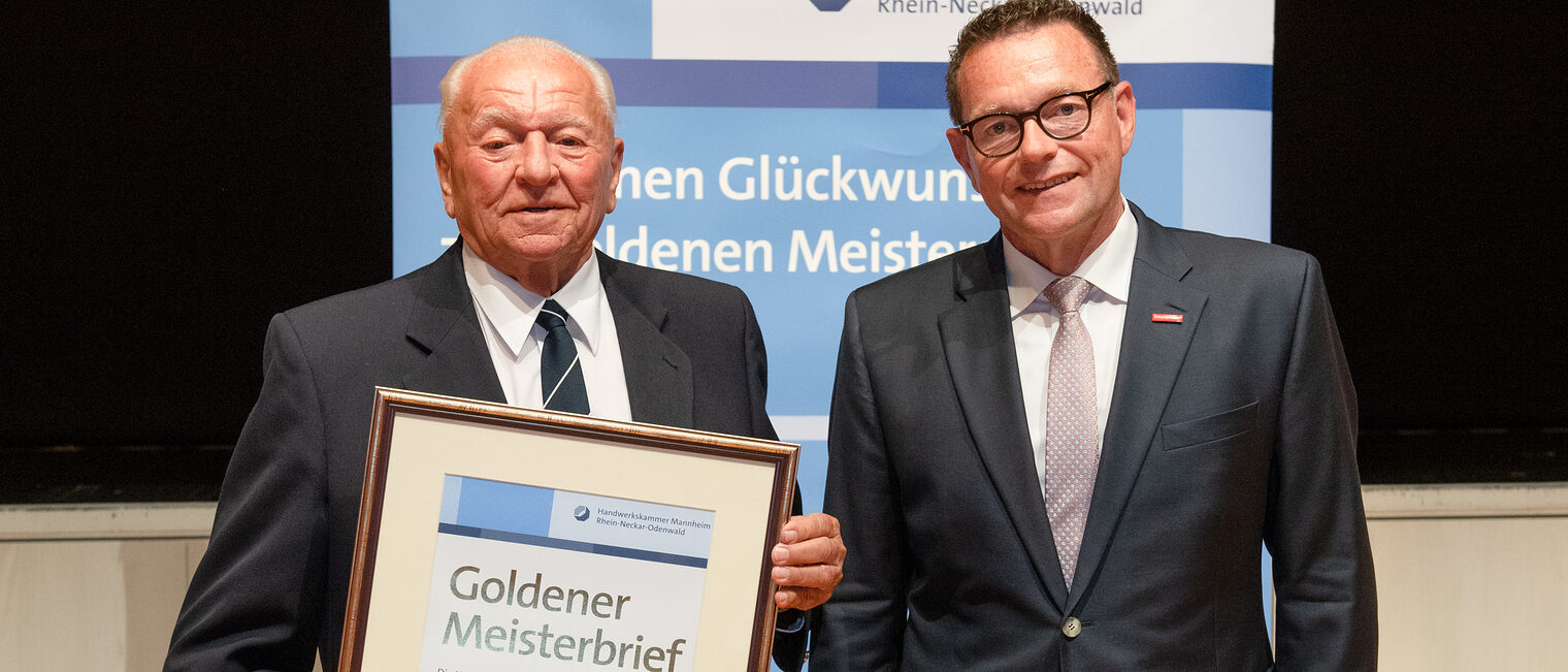 Kammerpräsident Klaus Hofmann überreicht Stuckateurmeister Hermann Smrcek auf der Goldene Meisterfeier in Wiesloch 2022 seinen Goldenen Meisterbrief