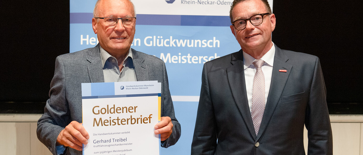 Kammerpräsident Klaus Hofmann überreicht Kraftfahrzeugmechanikermeister Gerhard Treibel auf der Goldene Meisterfeier in Wiesloch 2022 seinen Goldenen Meisterbrief