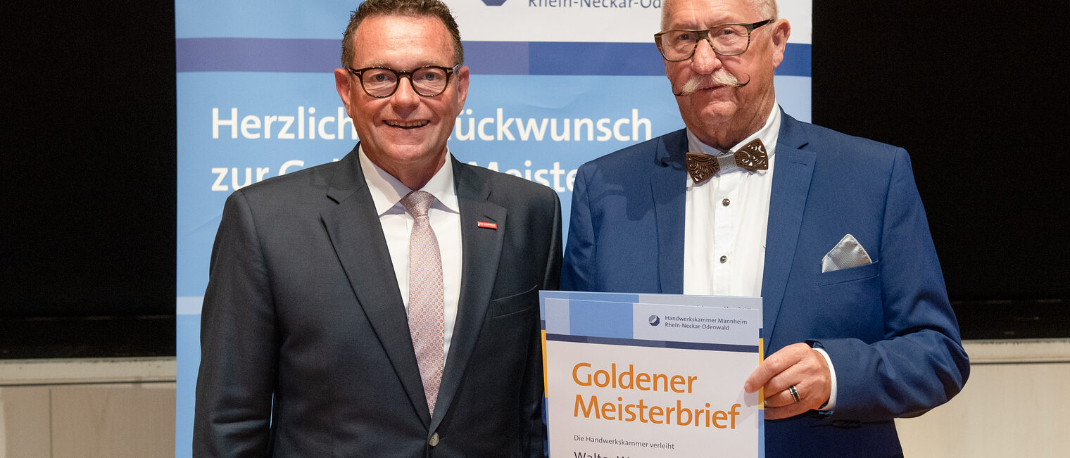 Kammerpräsident Klaus Hofmann überreicht Friseurmeister Walter Werner auf der Goldene Meisterfeier in Wiesloch 2022 seinen Goldenen Meisterbrief