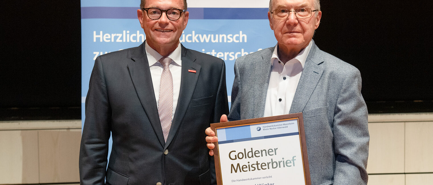 Kammerpräsident Klaus Hofmann überreicht Maschinenbauermeister Ferdinand Winter auf der Goldene Meisterfeier in Wiesloch 2022 den Goldenen Meisterbrief
