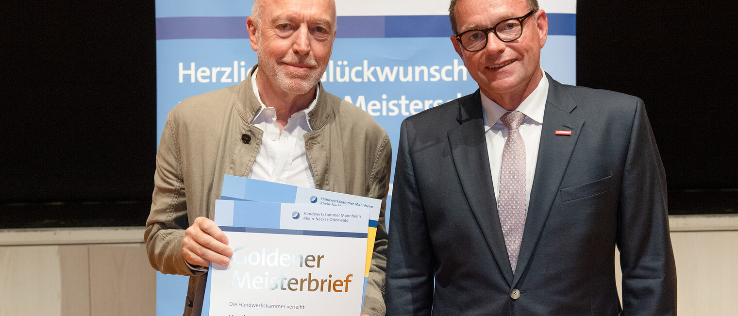 Kammerpräsident Klaus Hofmann überreicht Dachdeckermeister Karl-Heinz Winterbauer auf der Goldene Meisterfeier in Wiesloch 2022 den Goldenen Meisterbrief