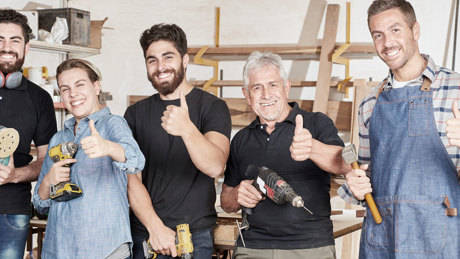 Gruppe von lächelnden Handwerkern. Alle halten den Daumen nach oben und halten ein Werkzeug in der anderen Hand.