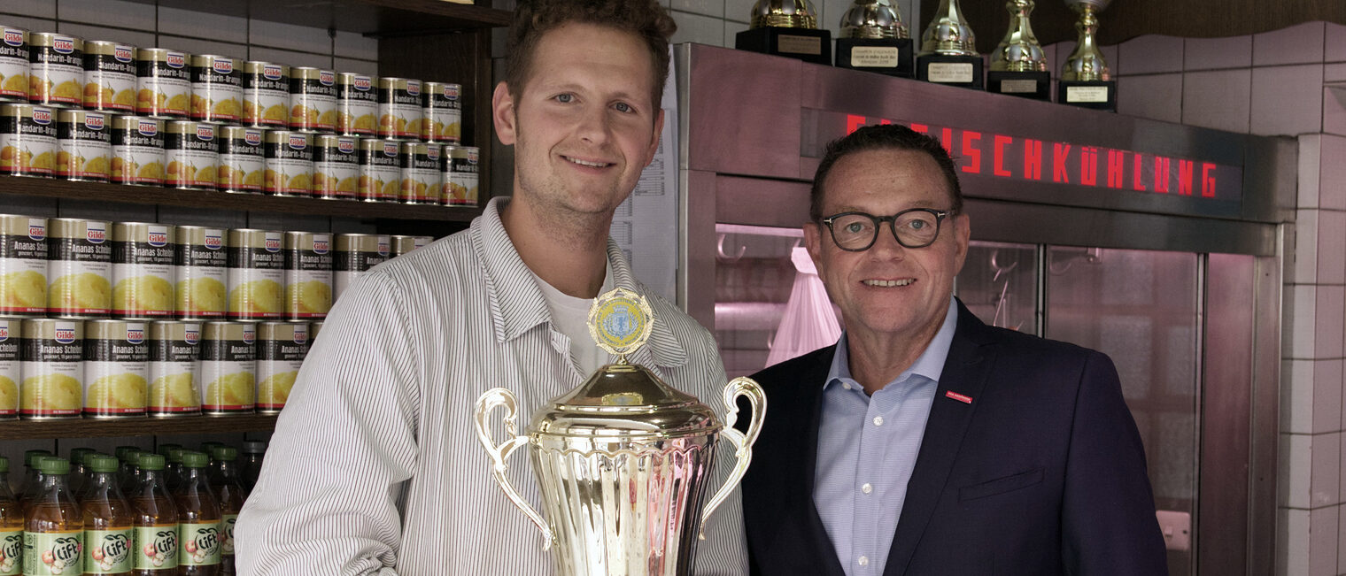 links: Philipp Burkhardt mit Pokal in den Händen und rechts Präsident Hofmann
